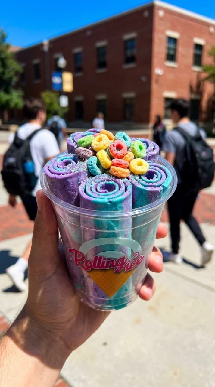 Purple and teal rolled ice cream topped with Froot Loops, held up on a sunny college campus