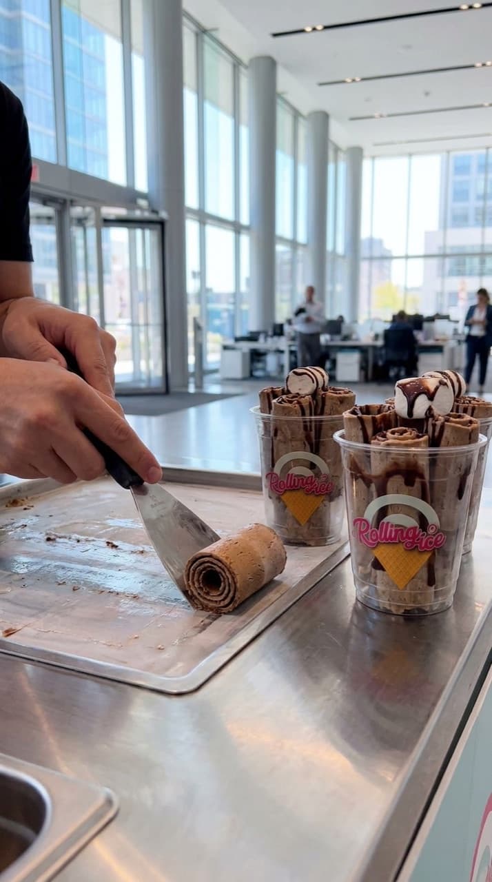 A spatula scraping coffee-flavoured ice cream into a roll on the frozen steel plate in an office lobby