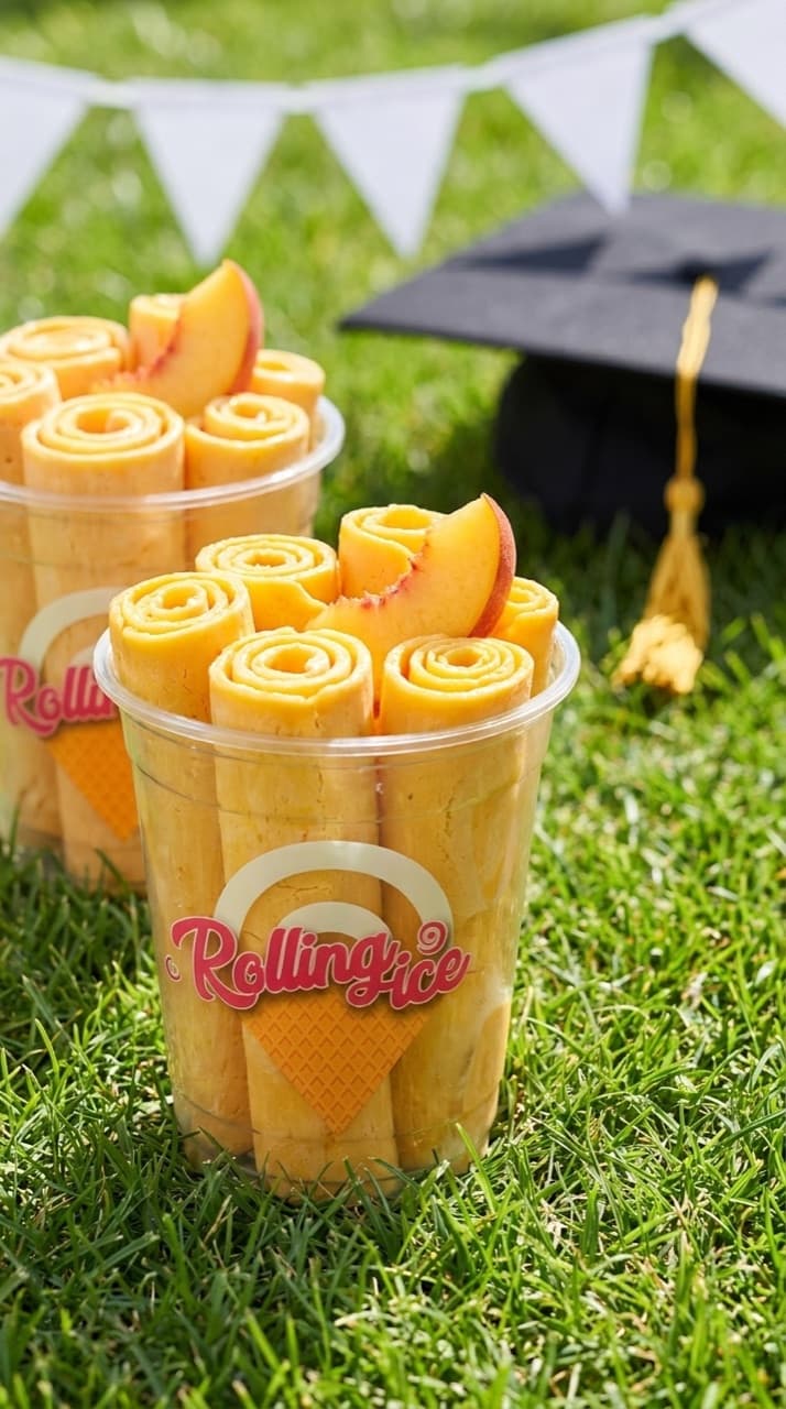 Mango rolled ice cream with fresh peach in branded cups on the grass beside a graduation cap