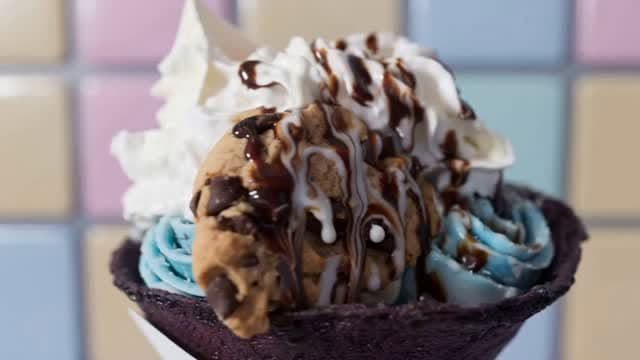 Cookie dough and blue rolled ice cream in a chocolate waffle bowl with whipped cream and chocolate drizzle