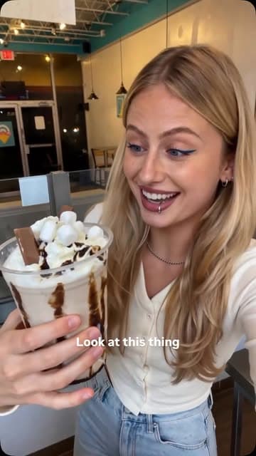 A customer holding a tall milkshake topped with marshmallows and a chocolate bar